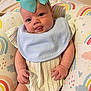 Laylah joined the competition — help win amazing prizes! baby, infant, bow, blue_bow, tongue_out, cute, smiling, face, hands, striped_outfit, bib, cushion, rainbow_pattern, colorful, soft_texture, indoors, child, playful, portrait, closeup