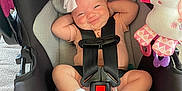 Laylah is registered to the contest to win money with this photo: baby, car_seat, smiling, bow, infant, toy, unicorn, plush, socks, straps, seatbelt, cute, child, indoor, car_seat_warning, pink, black, gray, comfort, happy