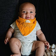 Anthony joined the competition — help win amazing prizes! baby, infant, child, bib, orange_bib, onesie, sitting, cute, portrait, indoor, skin, face, hands, feet, expression, clothing, fabric, soft_toys, blanket, dark_background