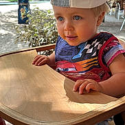 Sacha participe au concours pour gagner de l'argent avec cette photo : toddler, child, high_chair, cap, shirt, wooden_furniture, outdoor, daylight, tree, leafy, curious, blue_eyes, shorts, striped_shorts, hand, face, portrait, sunlight, summer, nature