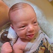 Nova is registered to the contest to win money with this photo: baby, infant, newborn, bathtub, bubbles, towel, foam, water, bath_time, face, head, hand, smile, tongue, skin, closeup, cloth_pattern, sunflower_pattern, happy, relaxed