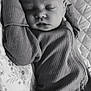 baby, sleeping, onesie, ribbed_clothing, blanket, floral_pattern, quilted, black_and_white, infant, peaceful, resting, portrait, close_up, face, head, arms, cozy, soft_lighting, indoor, cute