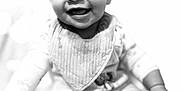 Calliah joined the competition — help win amazing prizes! baby, infant, smile, happy, face, bib, clothing, person, child, portrait, black_and_white, cute, sitting, young, small, cute_expression, indoors, soft_light, closeup, joyful