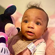 Calliah joined the competition — help win amazing prizes! baby, child, plush_toy, minnie_mouse, pink_clothing, bib, curly_hair, wide_eyes, indoor, soft_lighting, cute, portrait, infant, toy, young_child, candid, expression, holding, warm_colors, cozy