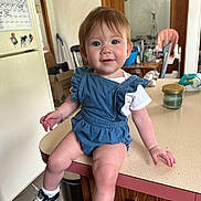 Nova is registered to the contest to win money with this photo: toddler, child, denim_romper, sneakers, converse, kitchen, counter, table, chair, refrigerator, calendar, bottle, candle, wood_cabinet, floor, indoor, smiling, face, person, clothing