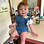 toddler, child, denim_romper, sneakers, converse, kitchen, counter, table, chair, refrigerator, calendar, bottle, candle, wood_cabinet, floor, indoor, smiling, face, person, clothing