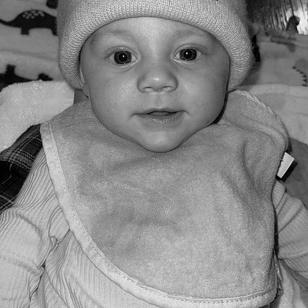 Lenny is registered to the contest to win money with this photo: baby, beanie, bib, black_and_white, child, closeup, clothing, cute, expression, eyes, face, hat, headwear, indoor, infant, mouth, person, portrait, soft_texture, young