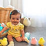 baby, blue_hair_clip, child, cute, decor, easter_eggs, floor, happy, indoor, infant, pastel_colors, playful, portrait, smile, socks, soft_light, stuffed_chicks, toy, wicker_basket, yellow_romper