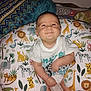baby, smiling, child, pillow, animal_pattern, white_shirt, indoor, blanket, happy, cute, infant, person, seated, colorful, young_child, portrait, cozy, home, mammal, skin