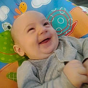Legend is registered to the contest to win money with this photo: baby, infant, smile, laughing, face, hands, gray_clothing, playmat, colorful, frog, snail, cartoon, pattern, cheerful, cute, child, indoors, happy, young, closeup