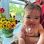 baby, child, pigtails, pink_bows, tongue_out, arms, window, flowers, yellow_flowers, red_flowers, green_vase, indoor, person, cute, playful, smiling, natural_light, face, happy, closeup