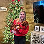 Boudreaux is registered to the contest to win money with this photo: woman, dog, dachshund, red_sweater, christmas_tree, holiday_decor, lights, bow, smile, indoor, wooden_wall, cabinet, photograph, framed_picture, furniture, festive, celebration, pet, holding, relaxed
