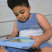 Washington is registered to the contest to win money with this photo: afro_hair, bed, blue_case, casual, child, clothing, device, focused, hand, headboard, indoors, portrait, shorts, sitting, skin, sock, tablet, technology, toddler, young