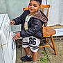 boy, chair, child, clothing, concrete, daylight, door, footwear, glass, jacket, outdoor, patio, person, plant, playful, shoes, shorts, smile, standing, washing_machine