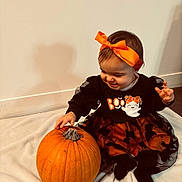 Victoire a rejoint le concours — aidez-le/la à gagner de superbes lots ! baby, child, toddler, pumpkin, halloween, orange_bow, black_dress, smiling, indoor, blanket, wall, floor, cute, festive, holiday, sitting, person, happy, headband, celebration