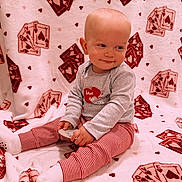 Karson is registered to the contest to win money with this photo: baby, child, infant, smile, sitting, blanket, playing_cards, hearts, striped_pants, grey_top, toy, cozy, cute, indoor, soft, comfortable, red, white, patterned, happy
