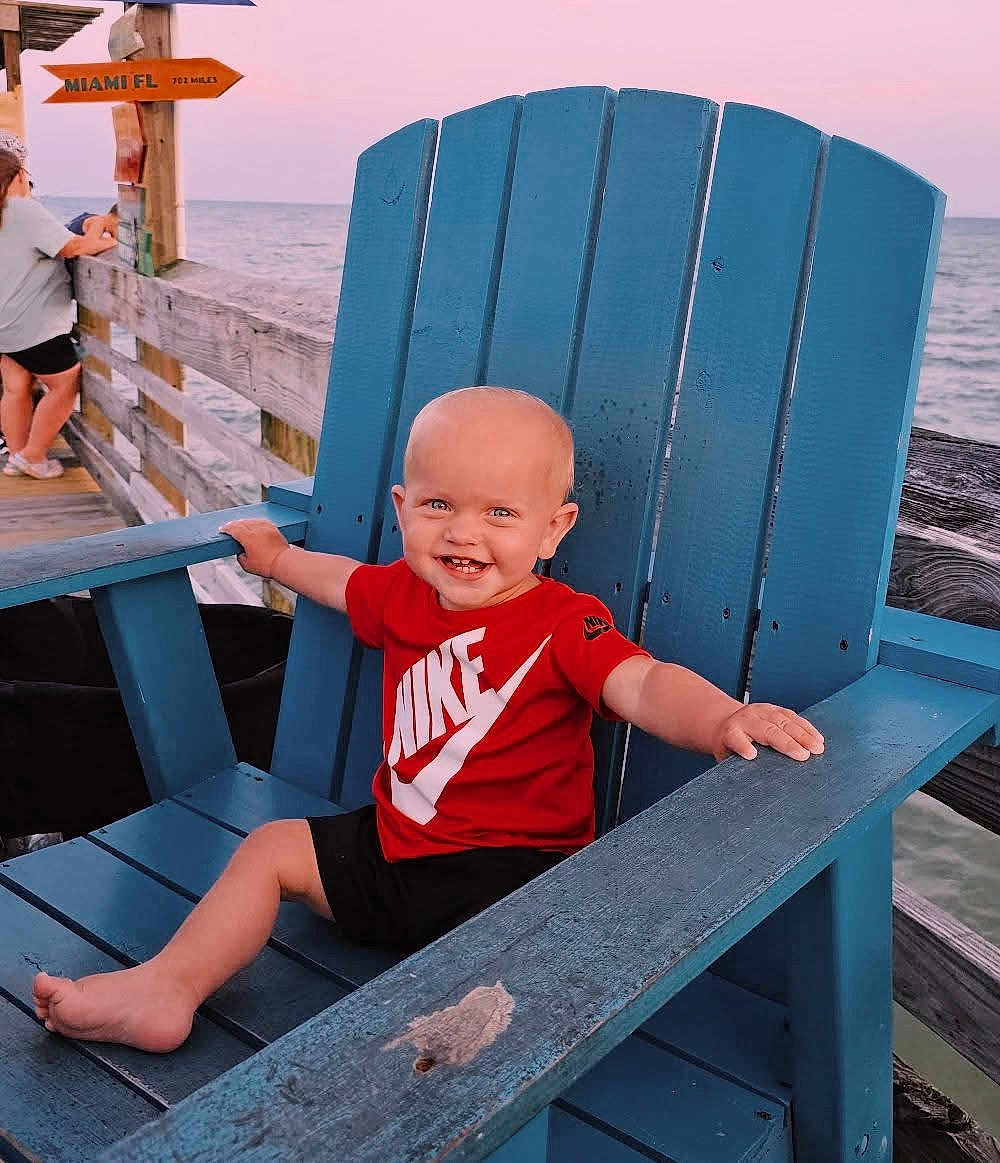 Karson joined the competition — help win amazing prizes! toddler, child, smiling, red_shirt, nike_logo, blue_chair, wooden_chair, pier, ocean, sea, sunset, outdoor, barefoot, happy, baby, person, summer, vacation, casual_clothing, water