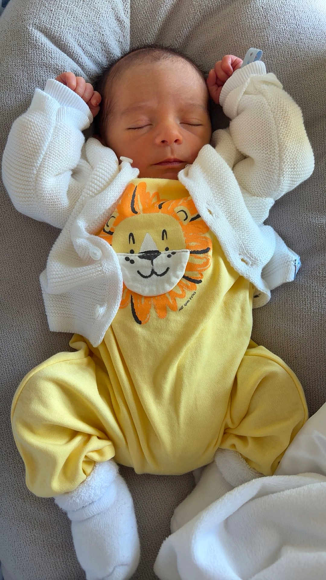 Lior participe au concours pour gagner de l'argent avec cette photo : baby, sleeping, yellow_outfit, white_cardigan, lion_design, socks, infant, cozy, soft_texture, cute, relaxed, child, portrait, indoors, blanket, resting, newborn, hands_up, clothing, sleep
