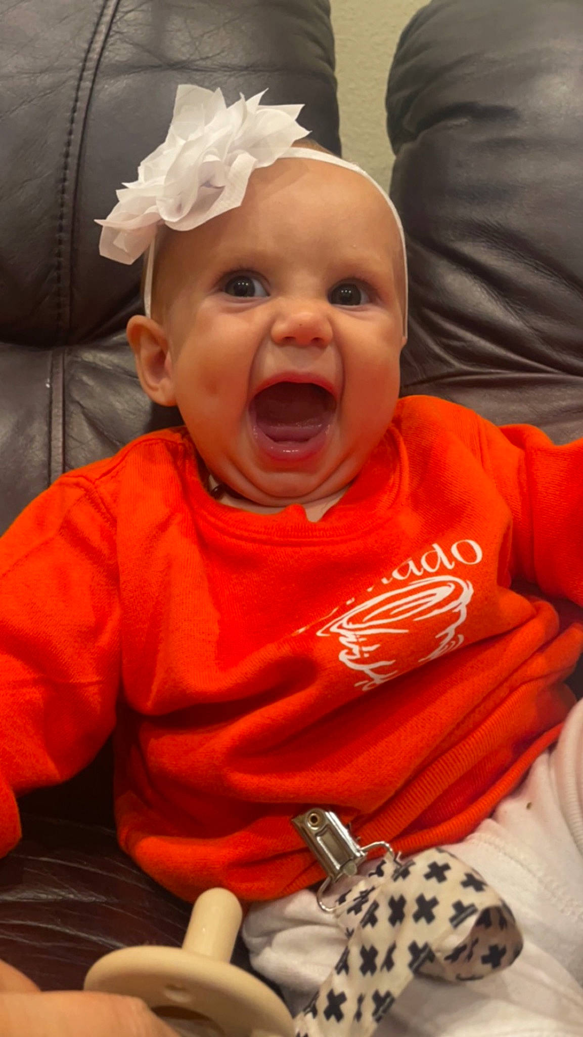 Hailyn is registered to the contest to win money with this photo: baby, baby_toddler_clothing, chair, cheek, child, comfort, fun, happy, laugh, mammal, mouth, nose, orange, person, sitting, sleeve, smile, tableware, toddler, toy