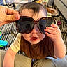 baby, child, sunglasses, hand, indoor, playtime, curious, expression, face, clothing, person, living_room, furniture, couch, toy, blanket, floor, skin, head, eyes