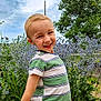 child, boy, smiling, garden, flowers, purple_flowers, greenery, outdoor, nature, plants, tree, fence, colorful_fence, sky, cloudy_sky, shirt, striped_shirt, happy, portrait, daylight