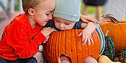Joel is registered to the contest to win money with this photo: baby, child, pumpkin, carved_pumpkin, autumn, fall, gourds, porch, smiling, cute, hat, orange_shirt, sitting, legs, feet, wooden_floor, outdoor, siblings, playing, cozy