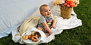 Skyler is registered to the contest to win money with this photo: baby, child, grass, blanket, donuts, flowers, basket, plate, smiling, outdoor, happy, sitting, food, nature, cute, portrait, toddler, clothing, knit_blanket, daylight