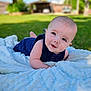 Skyler is registered to the contest to win money with this photo: baby, blanket, blue_clothing, outdoor, grass, smiling, infant, cute, portrait, face, child, soft_texture, toddler, happy, sunny, nature, head, eyes, skin, lying_down