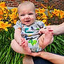 Skyler joined the competition — help win amazing prizes! baby, infant, smiling, dinosaur_onesie, yellow_flowers, lilies, green_leaves, brick_wall, outdoor, person, happy, cute, toes, hands, legs, nature, garden, child, portrait, summer