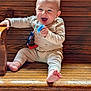 baby, child, pacifier, wooden_bench, smiling, happy, indoor, pajamas, barefoot, infant, cute, seated, wood_texture, light_skin, short_hair, playful, one_person, holding_object, casual, relaxed