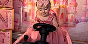 Karina is registered to the contest to win money with this photo: child, baby, toddler, pink, princess, castle_backdrop, toy_car, steering_wheel, pink_dress, headband, bow, birthday_party, balloon, decorations, stacked_blocks, glitter, portrait, indoor, celebration, smiling