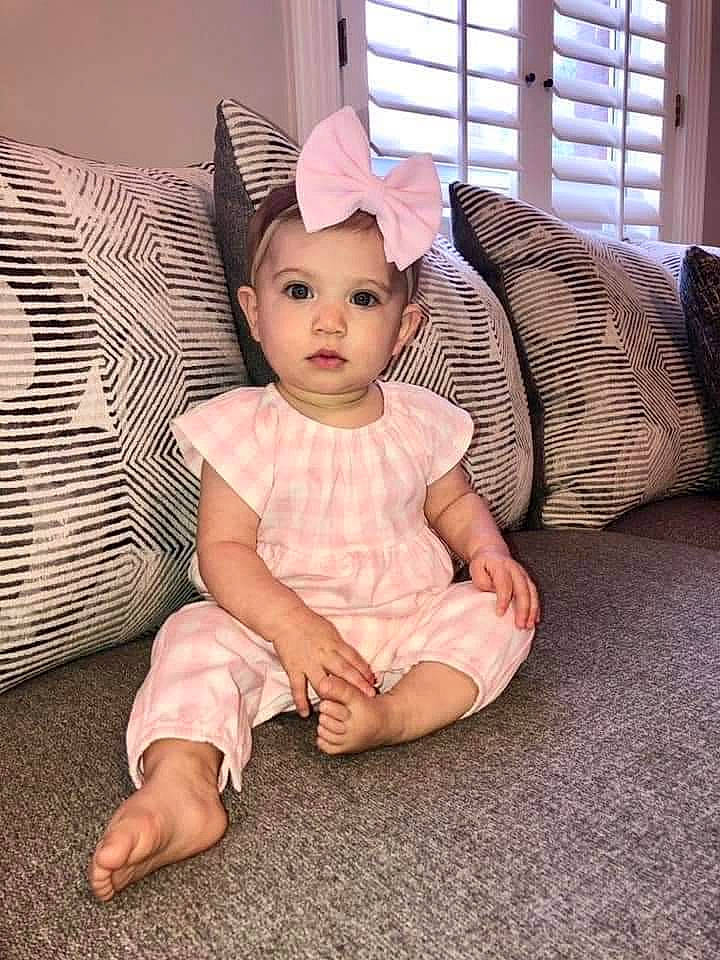 Nora is registered to the contest to win money with this photo: baby, baby_toddler_clothing, cap, comfort, costume_hat, couch, dress, eye, hairstyle, happy, head, headgear, headwear, pattern, person, pink, sleeve, sun_hat, t_shirt, toddler