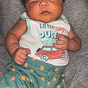 Knox is registered to the contest to win money with this photo: baby, infant, child, face, hair, clothing, tank_top, shorts, pattern, sun_pattern, car_print, fist, expression, laying, blanket, soft, skin, cute, indoors, portrait