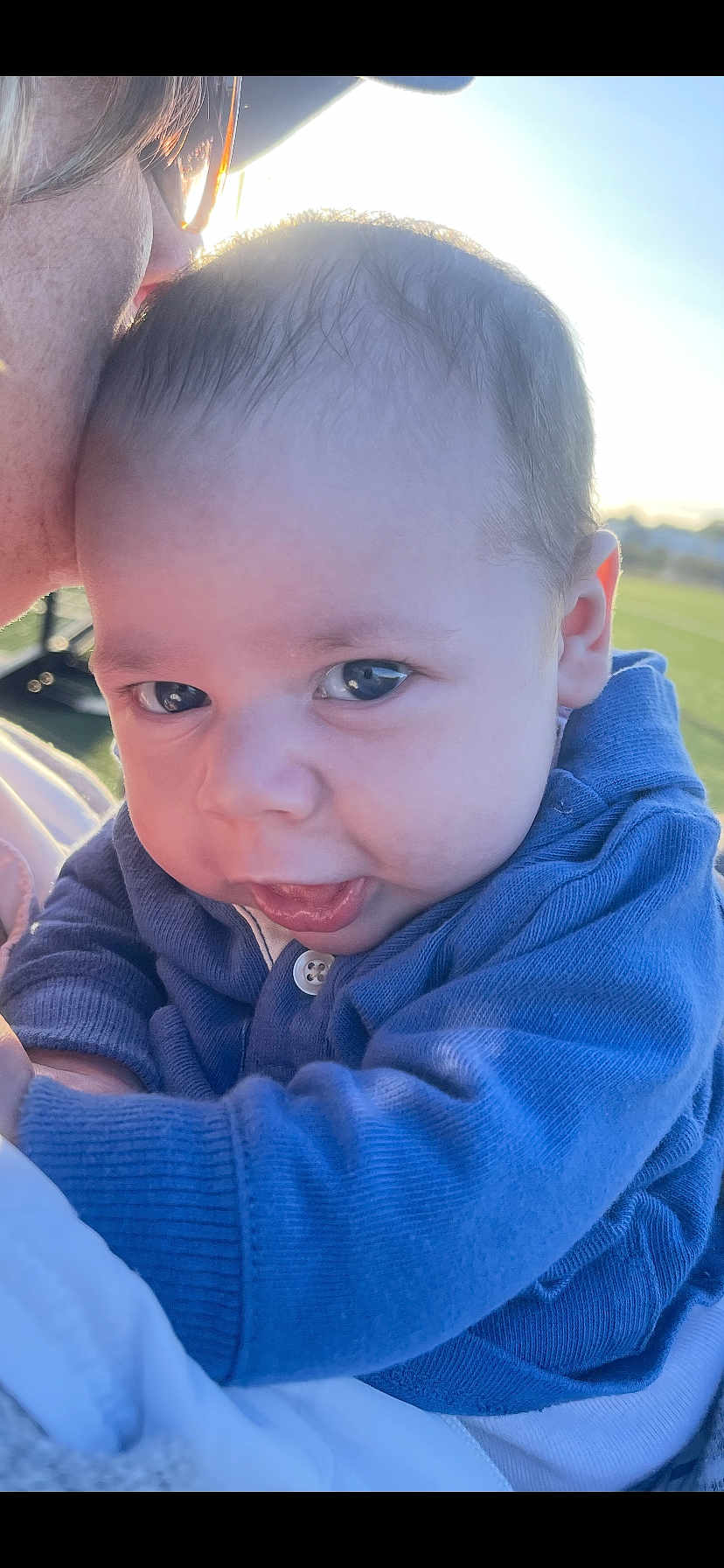 Asher is registered to the contest to win money with this photo: baby, child, face, portrait, close_up, blue_sweater, outdoor, daylight, person, skin, head, eyes, expression, infant, holding, warm_light, curious, cute, young, soft