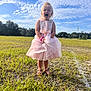 child, girl, dress, pink, grass, field, outdoor, sky, clouds, sunlight, footwear, sandal, bracelet, nature, young, person, daytime, casual, expression, standing