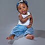baby, child, smiling, jeans, tank_top, barefoot, bracelets, hair_bows, curly_hair, studio, portrait, sitting, cute, happy, expression, skin, foot, fashion, accessory, one_person