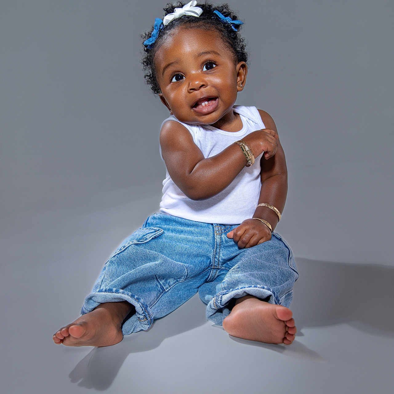 Leylani is registered to the contest to win money with this photo: accessory, baby, barefoot, bracelets, child, curly_hair, cute, expression, fashion, foot, hair_bows, happy, jeans, one_person, portrait, sitting, skin, smiling, studio, tank_top