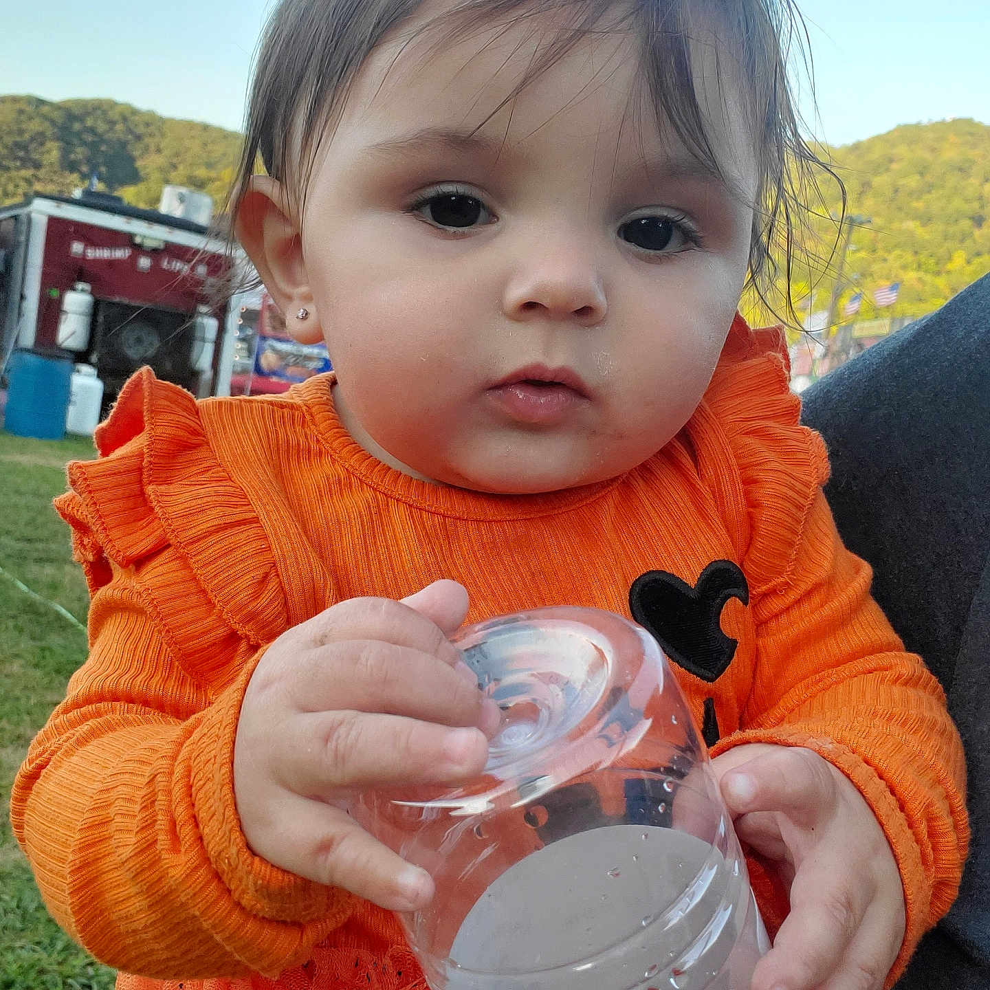 Nyla joined the competition — help win amazing prizes! baby, background, child, closeup, clothing, curious, daylight, earrings, face, fair, grass, hand, holding, nature, orange_sweater, outdoor, person, plastic_cup, portrait, toddler