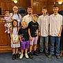 adults, braids, carpet, casual_clothing, children, diverse_ages, dresses, family, glasses, group, happy, indoor, people, portrait, semi_formal, shoes, shorts, smiling, standing, wood_paneling