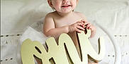 Ellie is registered to the contest to win money with this photo: baby, child, girl, smiling, wicker_chair, white, flower_headband, tutu, decor, one_sign, portrait, indoor, cute, happy, sitting, infant, celebration, soft_lighting, closeup, person