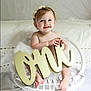 baby, child, girl, smiling, wicker_chair, white, flower_headband, tutu, decor, one_sign, portrait, indoor, cute, happy, sitting, infant, celebration, soft_lighting, closeup, person