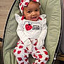 baby, infant, smiling, sitting, bouncer, headband, bow, ladybug_pattern, onesie, pajamas, white_clothing, red_accent, happy, portrait, face, hands, seat, indoor, playful, cute