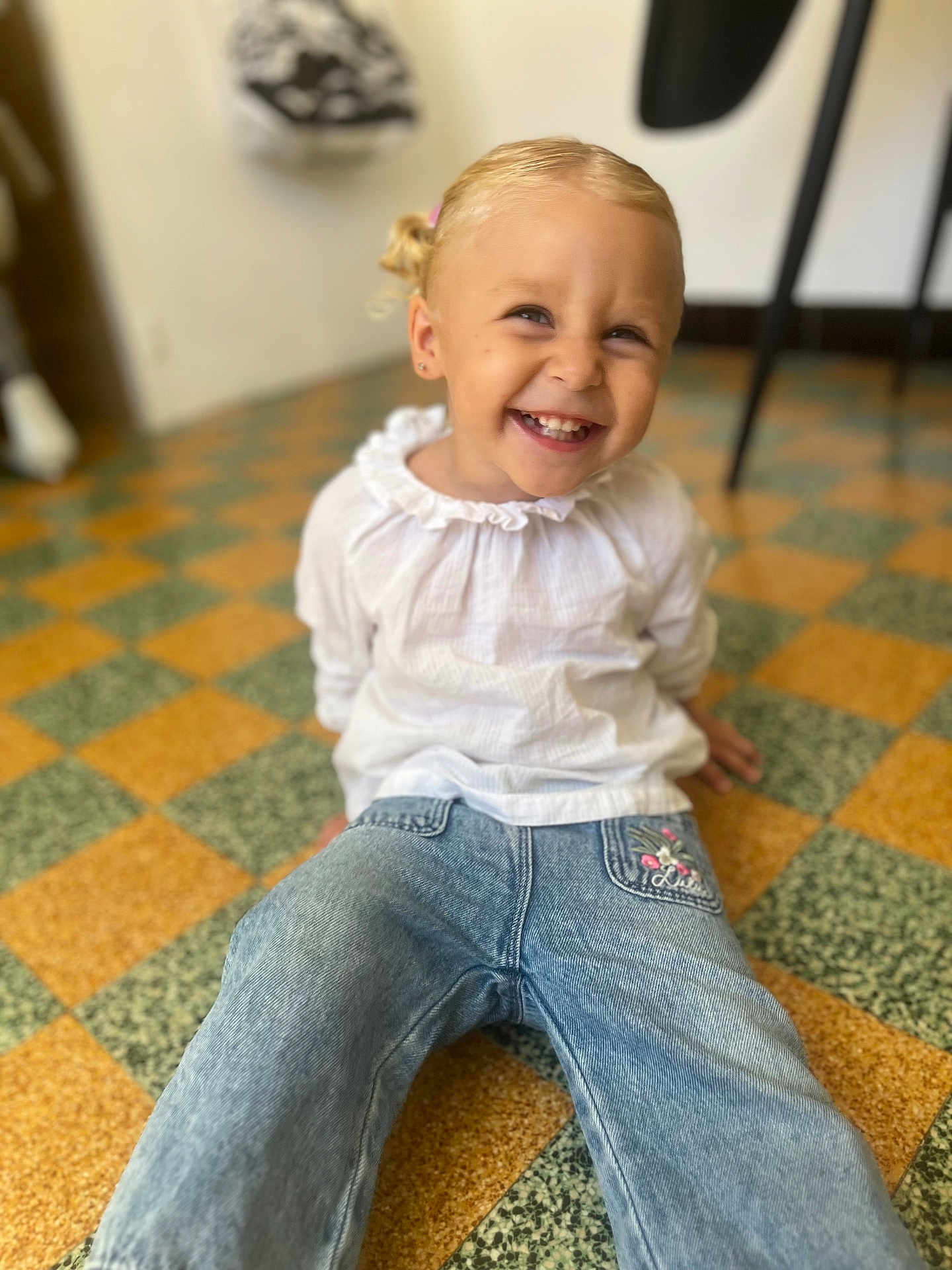 Elsa a rejoint le concours — aidez-le/la à gagner de superbes lots ! child, toddler, smiling, happy, indoor, floor, checkered_floor, jeans, white_top, blonde_hair, pigtails, sitting, casual_clothing, cute, portrait, young_child, person, fashion, playful, joy