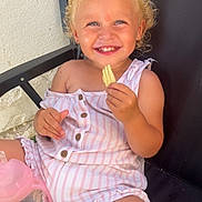 Elsa a rejoint le concours — aidez-le/la à gagner de superbes lots ! toddler, child, smiling, blonde_hair, curly_hair, pink_romper, striped_clothing, sitting, black_chair, snack, chip, happy, outdoor, sunlight, drink_container, sippy_cup, barefoot, buttoned_clothing, face, person