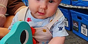 Sylas joined the competition — help win amazing prizes! baby, child, toy, dinosaur_toy, rocking_toy, blue, storage_bins, indoor, carpet, person, cute, overalls, wooden_handle, play, infant, sitting, curious, expression, floor, store