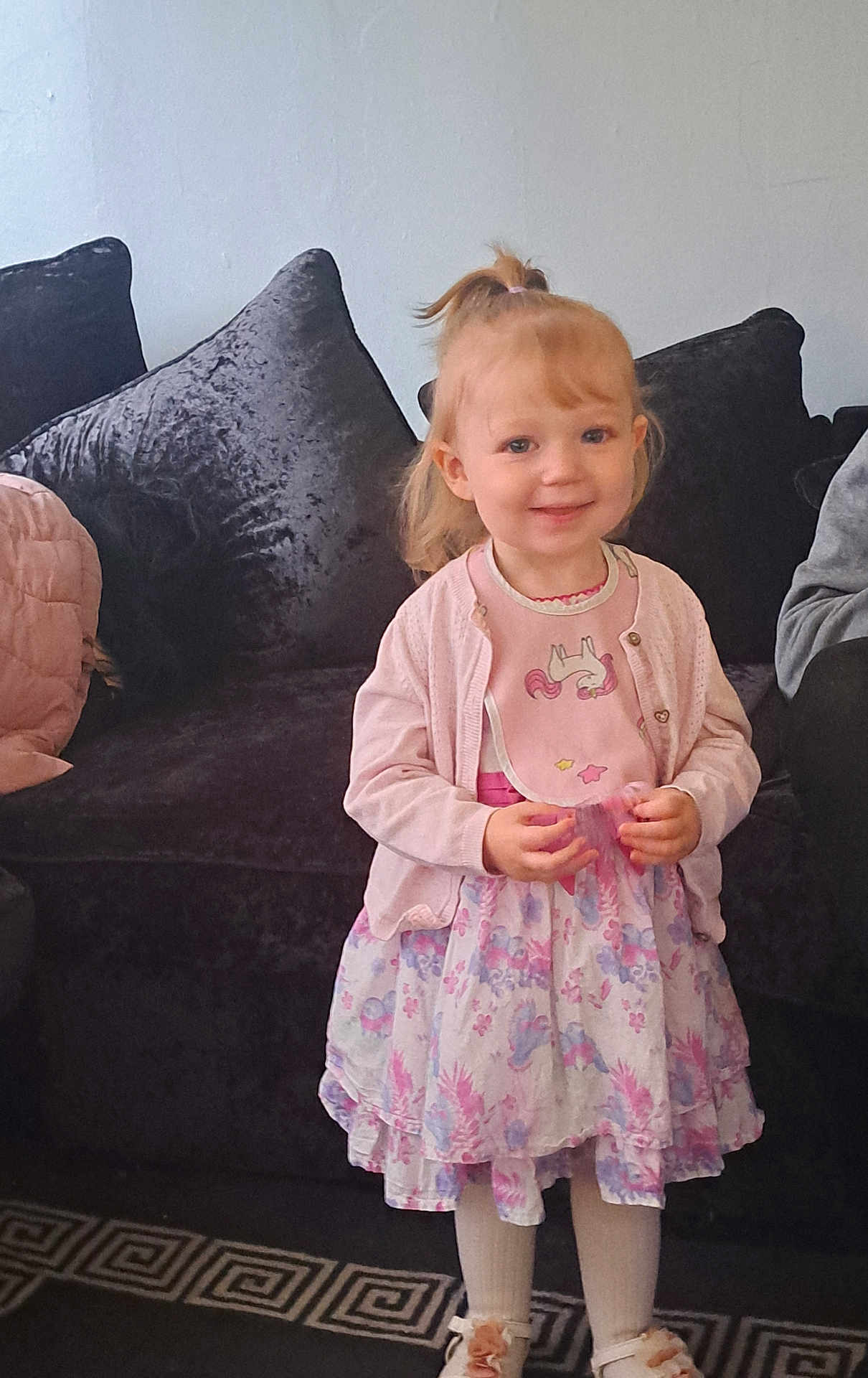 Nala-mai joined the competition — help win amazing prizes! toddler, child, girl, smile, standing, dress, floral, pink, bib, unicorn, pony_tail, couch, pillow, carpet, indoors, happy, clothing, person, cute, young