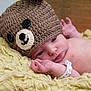 baby, infant, newborn, knitted_hat, button_eyes, bear_hat, blanket, yarn_texture, hospital_band, wristband, face, eyes, hand, chest, skin, portrait, cozy, sleepy, lying_down, cute