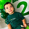 Liam Infante joined the competition — help win amazing prizes! toddler, child, green_clothing, shorts, tshirt, balloons, birthday, celebration, indoor, portrait, curly_hair, sitting, face, eyes, fuzzy_stool, decorations, number_two, happy, cute, person