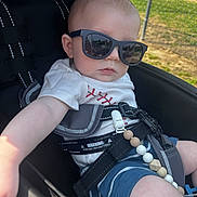 Devon joined the competition — help win amazing prizes! baby, child, sunglasses, stroller, outdoor, sunlight, clothing, shorts, tshirt, seatbelt, beads, hand, face, head, person, summer, shade, fence, grass, reflection