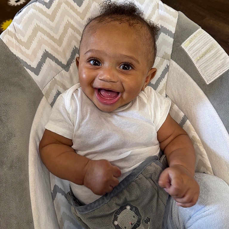 Nyzaun is registered to the contest to win money with this photo: animal_embroidery, baby, baby_chair, blanket, bright_eyes, chevron_pattern, child, comfortable, cozy, curly_hair, cute, happy, indoor, infant, light_blue_pants, playful, portrait, small_hands, smiling, white_shirt